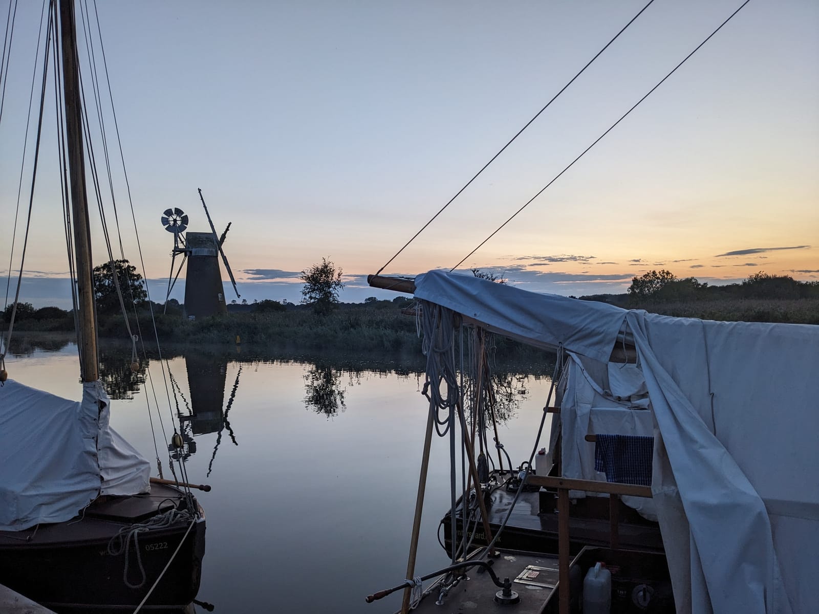 Moored boats at dusk with a Norfolk windmill silhouetted and reflected in still water
