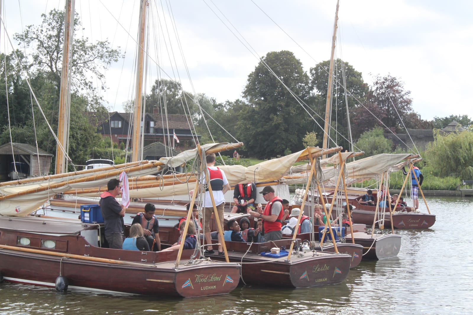 Several wooden half-deckers rafted together, crews and children sharing a break on the water